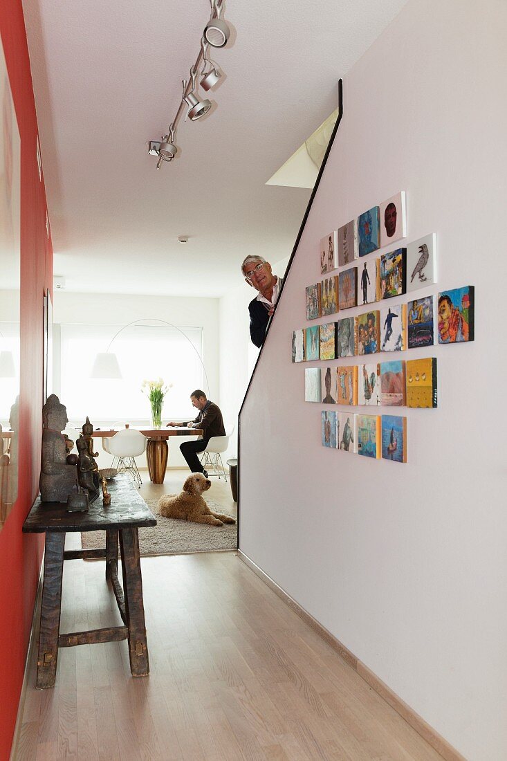 Rustikaler Holztisch gegenüber Bildersammlung an Wand des Treppenaufgangs, mit Mann, im Hintergrund Essplatz am Fenster