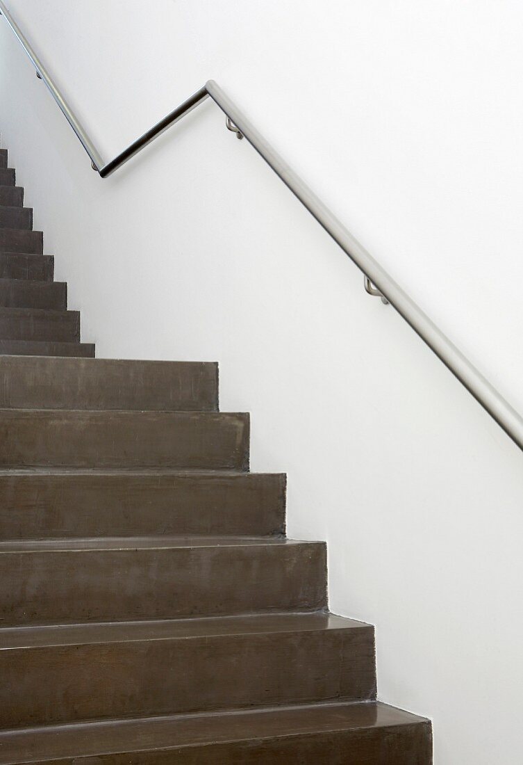 Staircase of dark grey, polished concrete with stainless steel handrail on wall