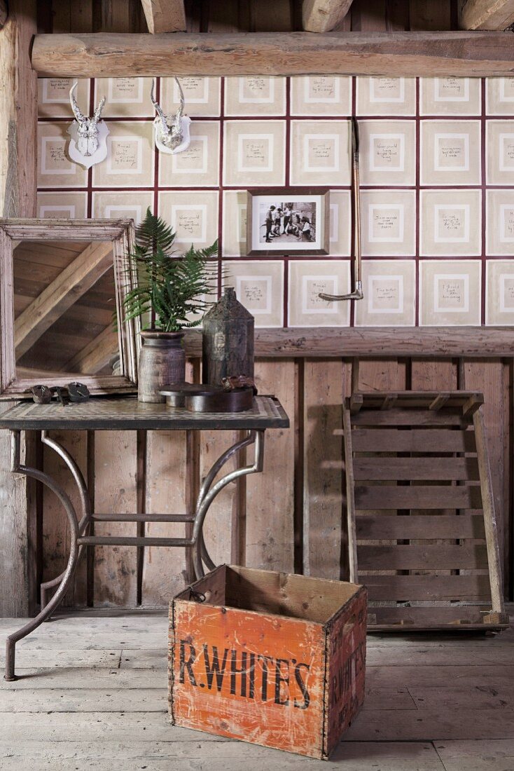 Old wooden crate in front of metal-framed side table and checked wallpaper in rustic attic interior