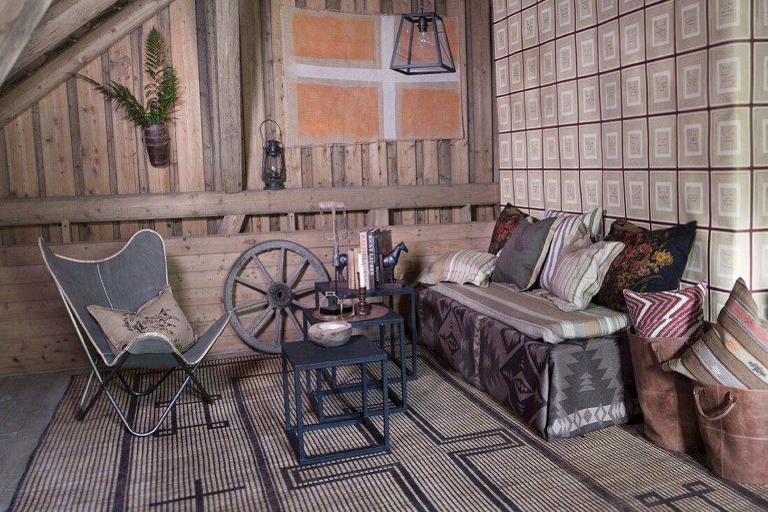 Butterfly armchair, metal side tables and comfortable bench with cushions against wall covered in vintage-look wallpaper