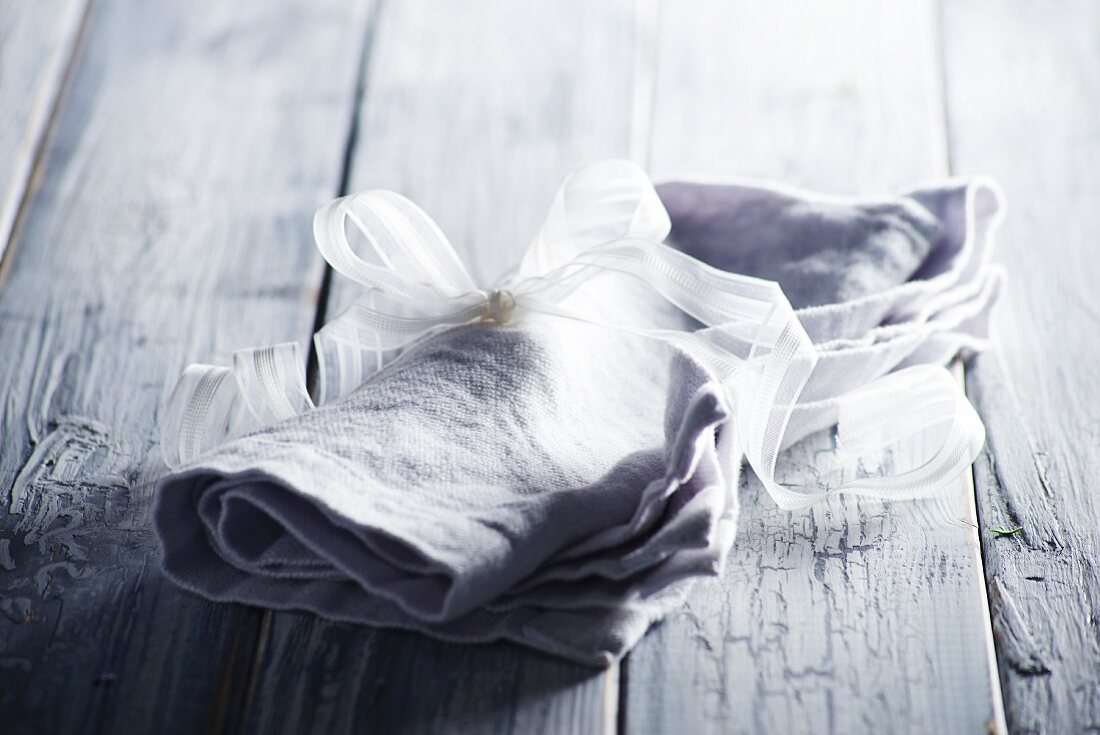 Grey linen napkin tied with white ribbon on wooden surface