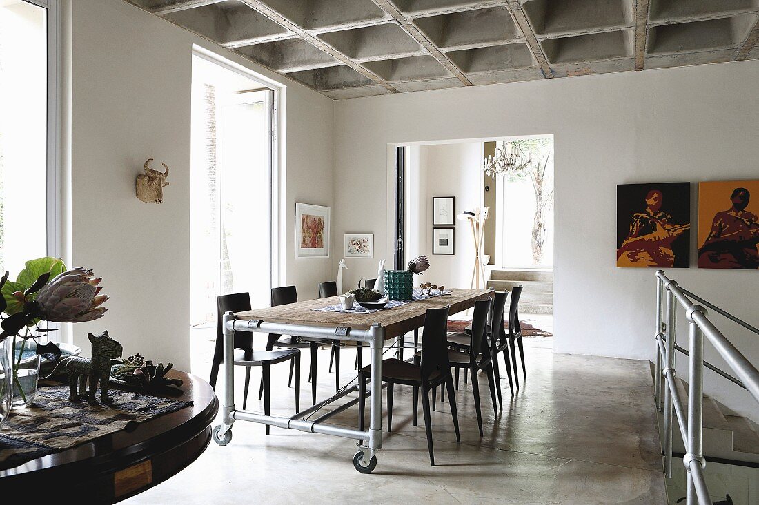 Dining table on castors with dark chairs opposite landing balustrade on open-plan gallery below concrete coffered ceiling