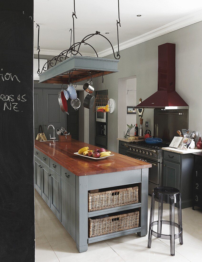 Grau lackierte Kücheninsel, darüber abgehängtes Gittergestell mit Kochutensilien, transparenter Kunststoff Barhocker, in einer Küche