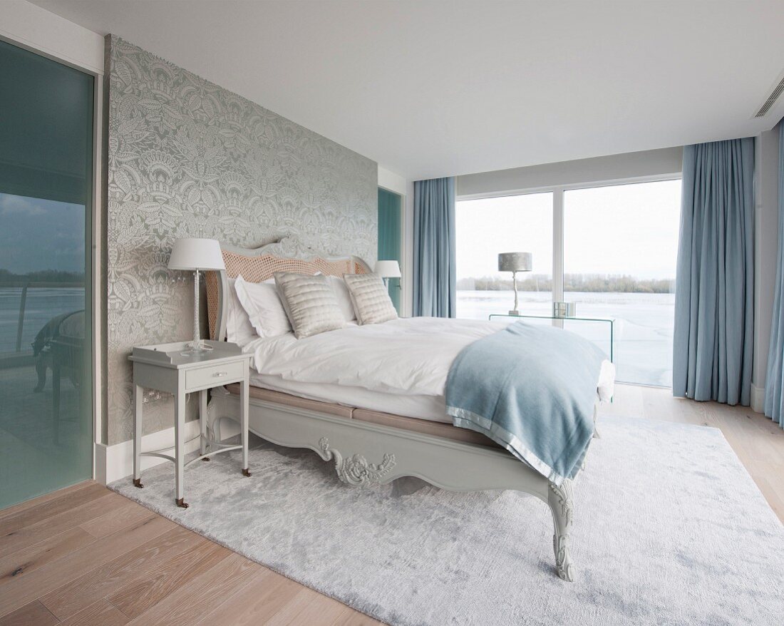 Doppelbett und Nachttisch vor Tapetenwand und Zugang zum Bad Ensuite in elegantem Schlafraum mit Seeblick
