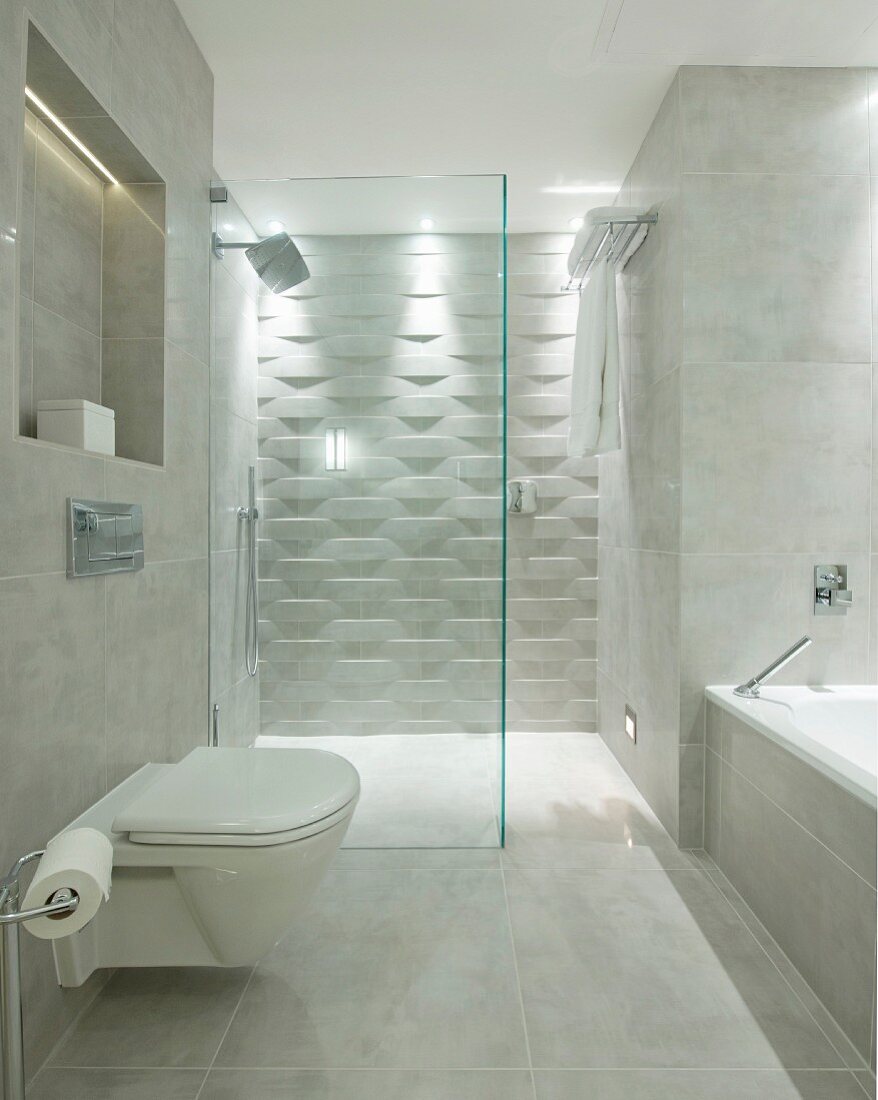 Toilet and bathtub in designer bathroom with marble tiles; walk-in shower with 3D structured tiles