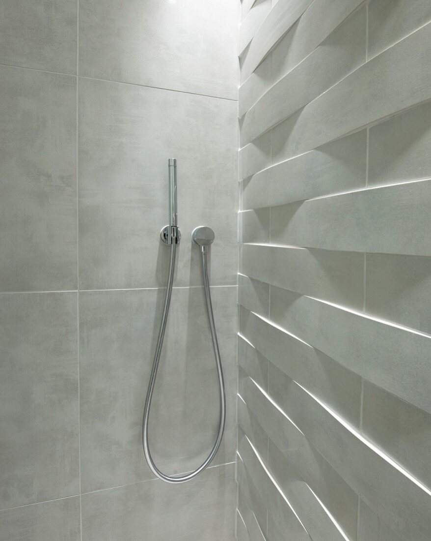 Modern, rod-shaped shower head mounted on marbled tiles in shower cubicle