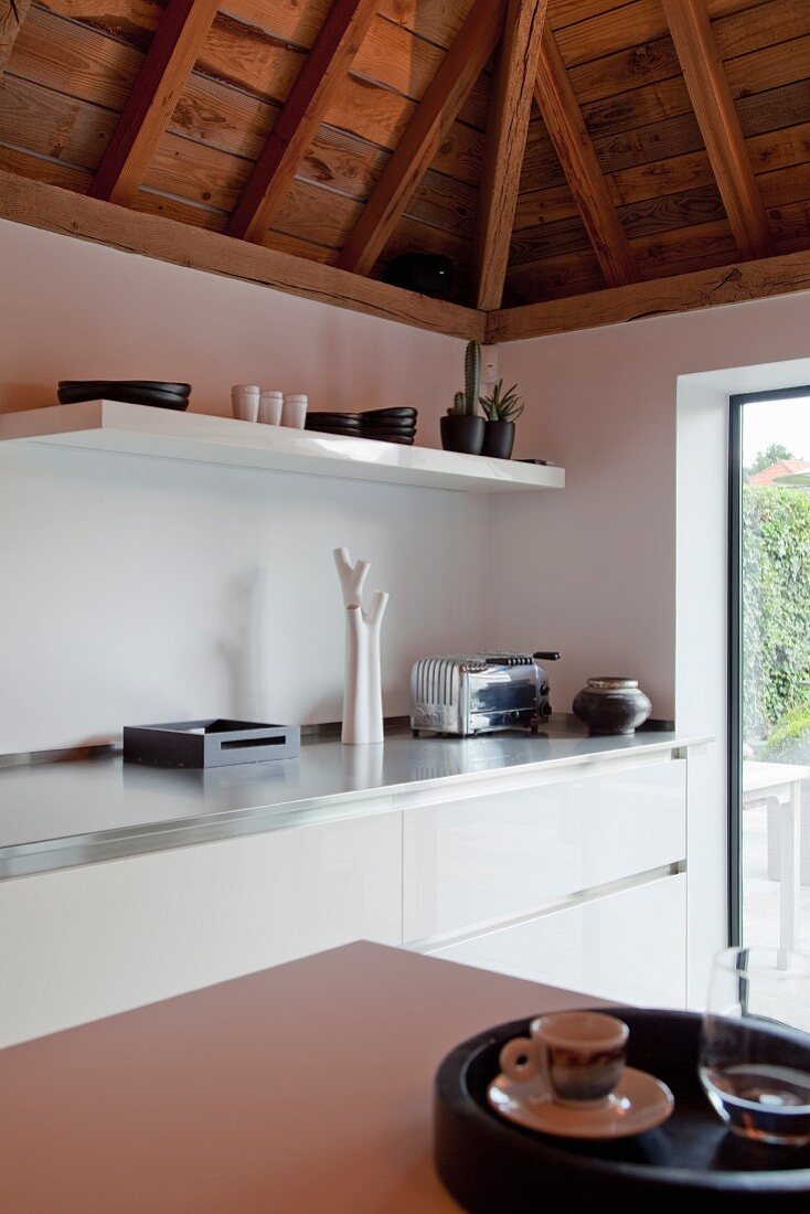 Corner of white designer kitchen with rustic roof structure
