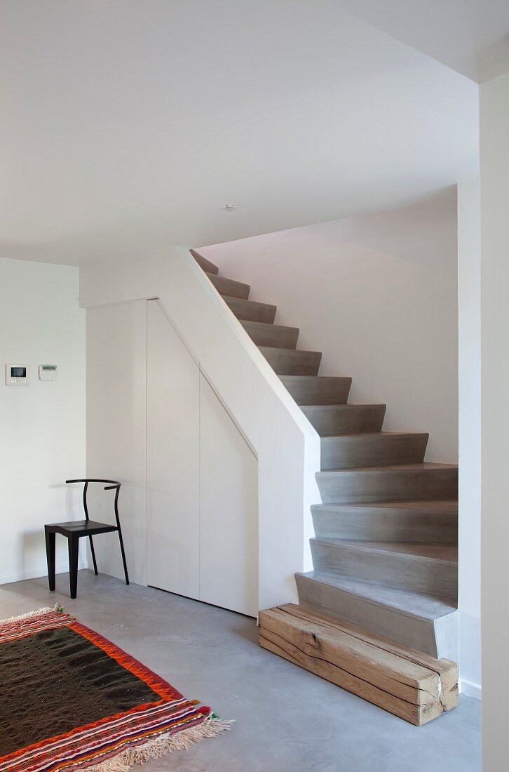 Concrete staircase with wooden starting step and fitted cupboards in spandrel in minimalist designer interior