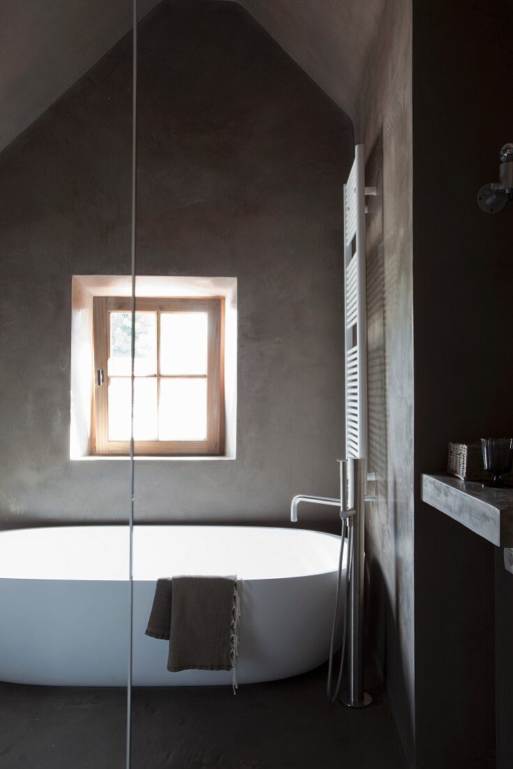 White designer bathtub with floor-mounted tap fittings in attic bathroom with lattice window