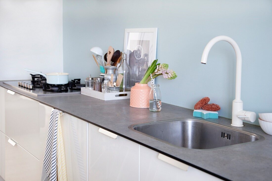 White kitchen counter with pale blue splashback, vase and kitchen utensils