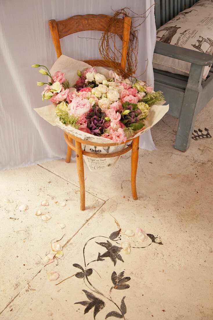 Holzstuhl mit Blumenstrauss in der Sitzfläche, davor auf Bodenmalerei mit floralem Motiv