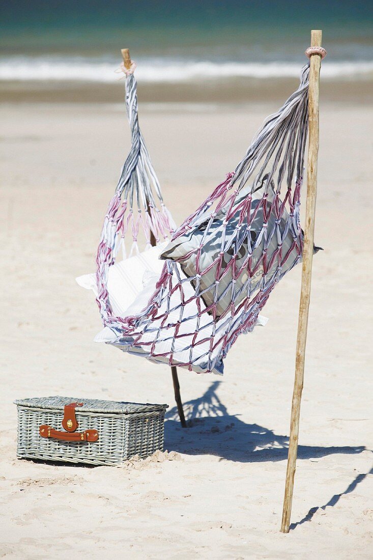 Hammock attached to sticks stuck in sandy beach next to picnic basket