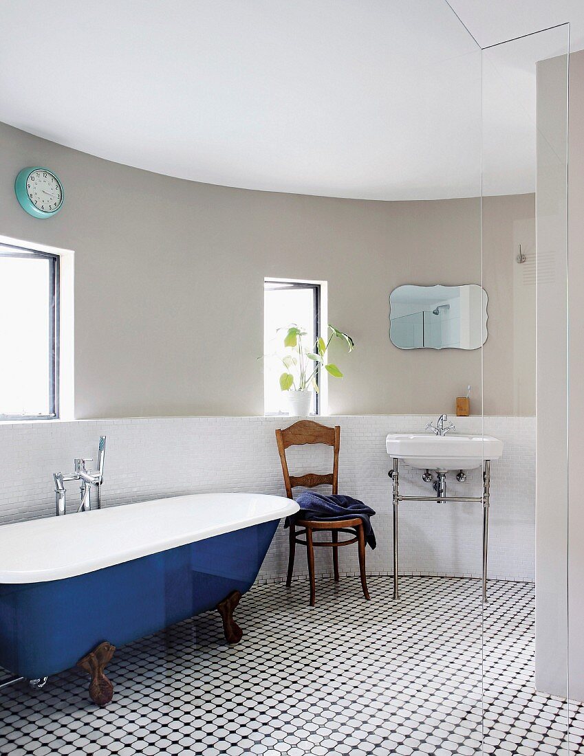 Blau lackierte Vintage Badewanne, Stuhl und Waschtisch an gebogener Wand im Bad mit schwarz-weißem Fliesenboden