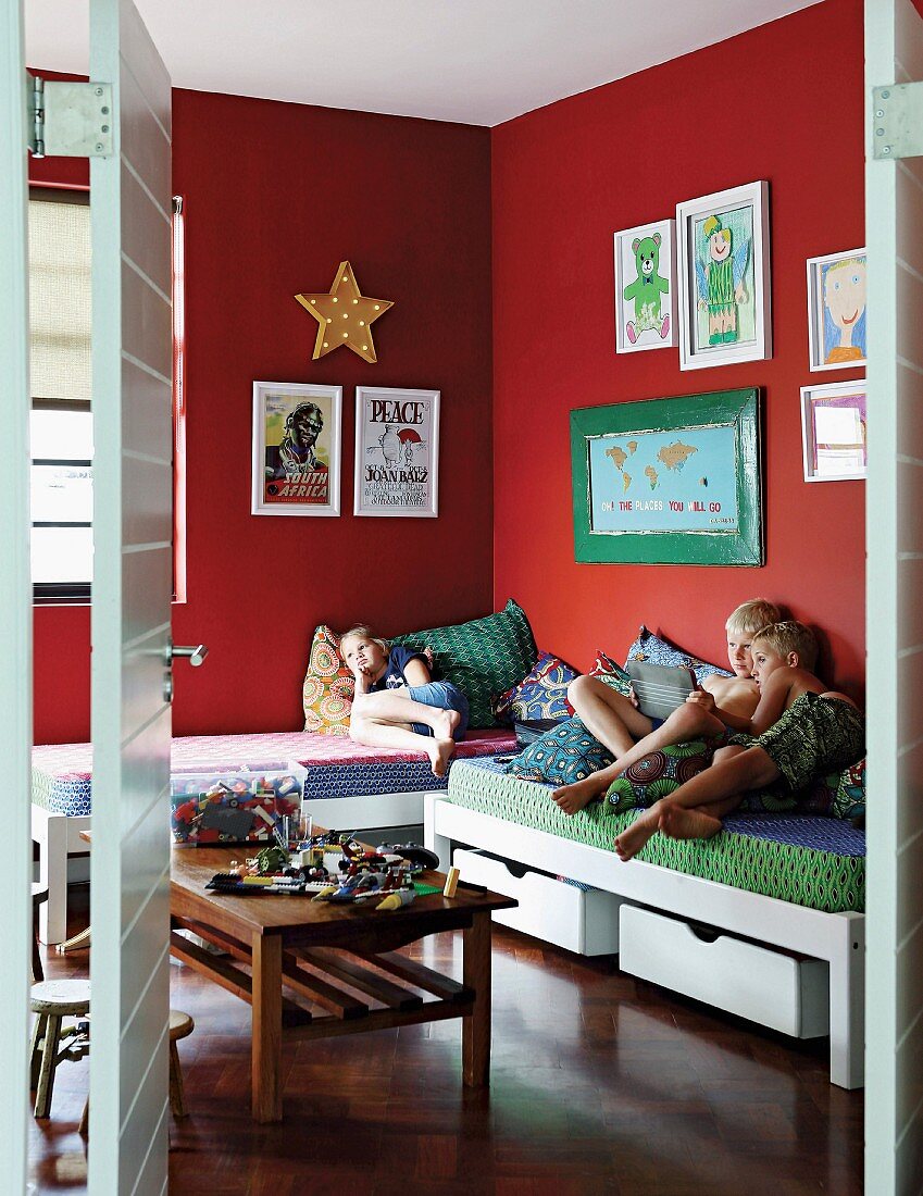 Kinder auf Betten im Kinderzimmer mit roten Wänden und aufgehängten Bildern