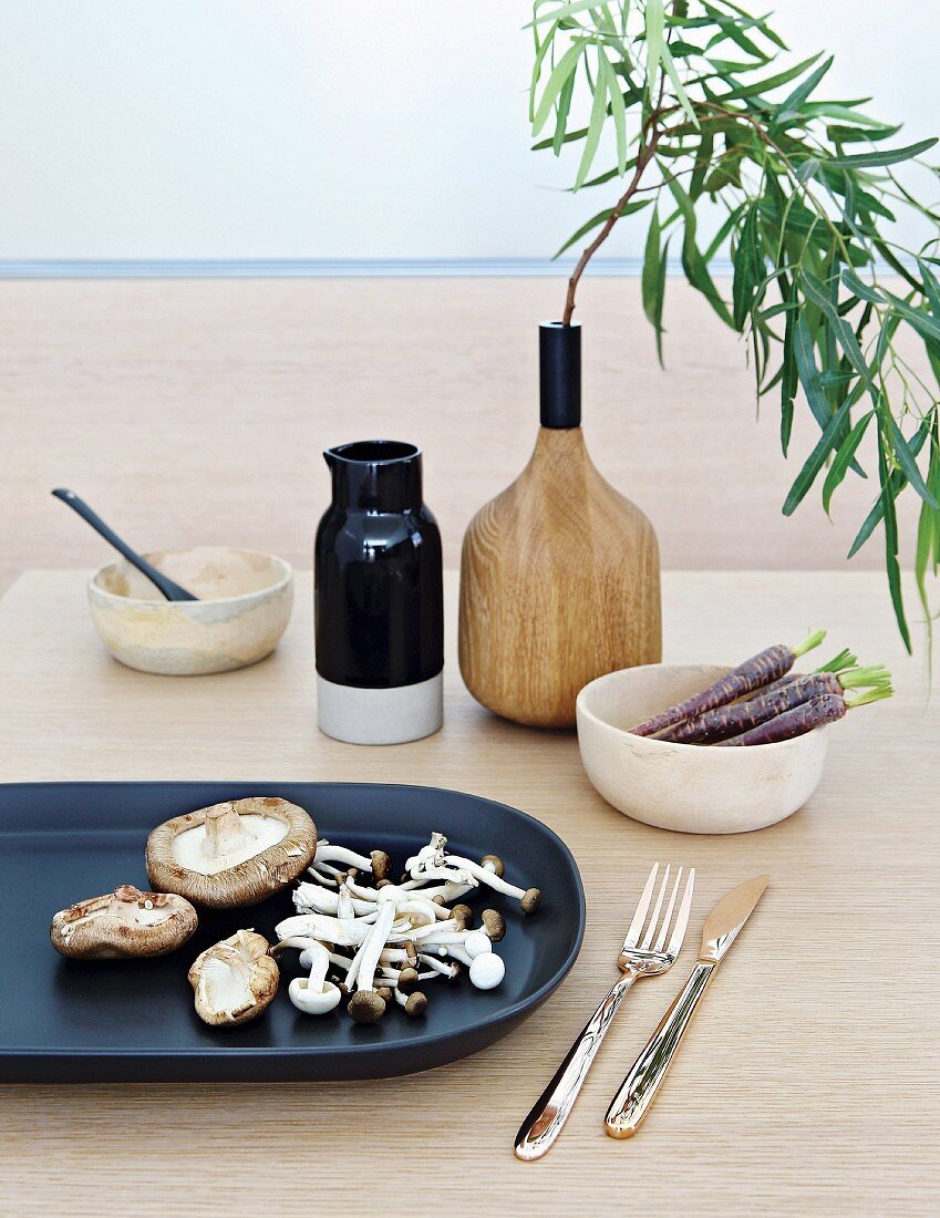 Schwarze Platte mit verschiedenen Pilzen, Schalen und Vase aus Holz mit Blätterzweig