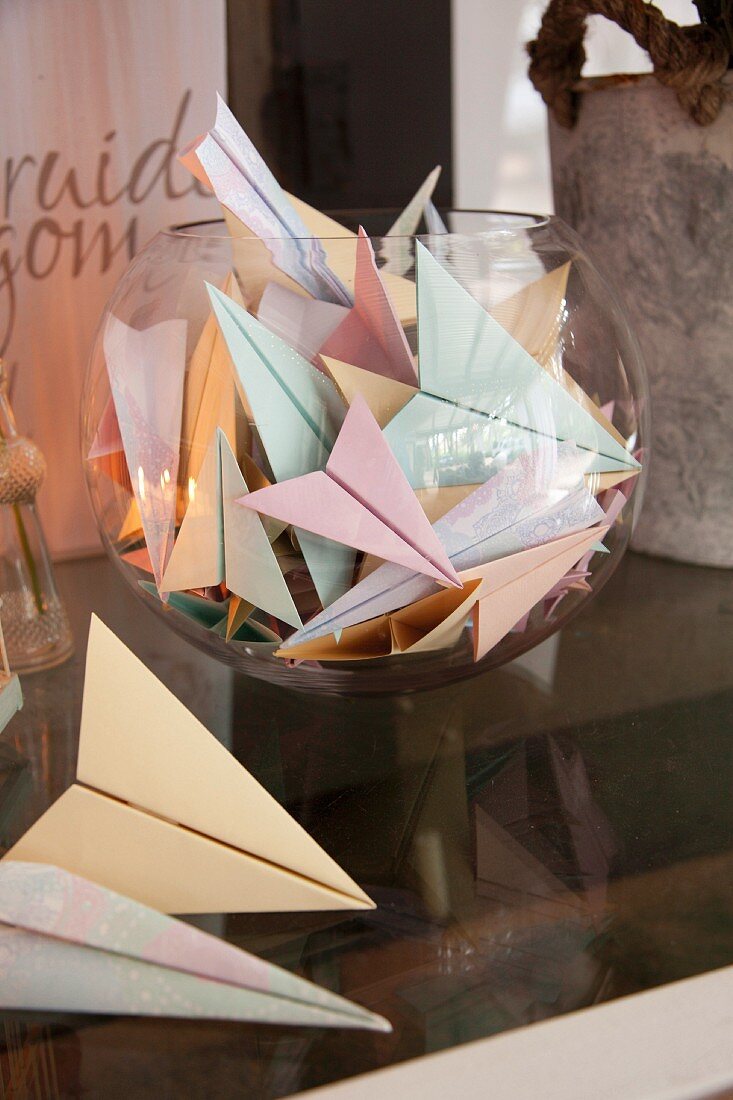 Gefaltete Papierflieger in verschiedenen Pastelltönen in Glasbehälter