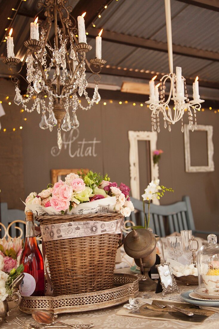 Roses in decorated basket on festively set table under lit candles in chandeliers