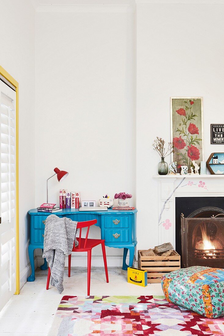 Blue-painted desk and red chair in niche next to fireplace