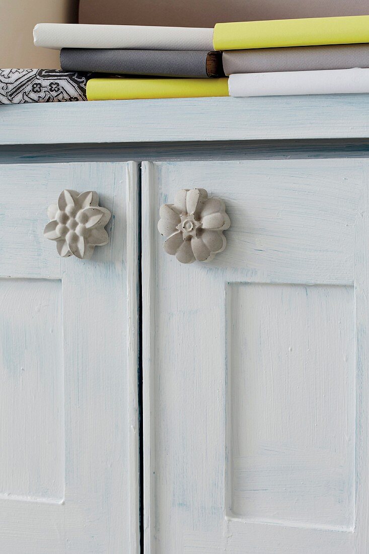 Möbelgriffe in Blütenform aus Beton an Türen eines hellgrau getönten Schränkchens