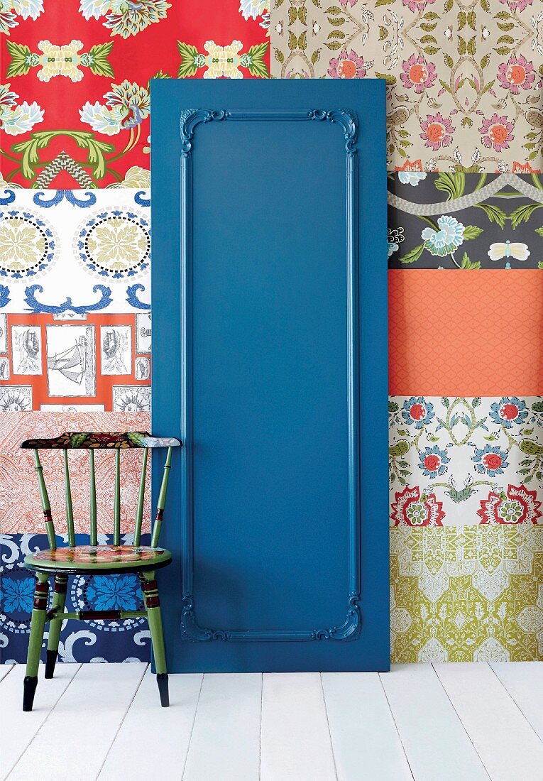 Blue-painted door with decorative moulding against wall covered in patchwork of different wallpapers