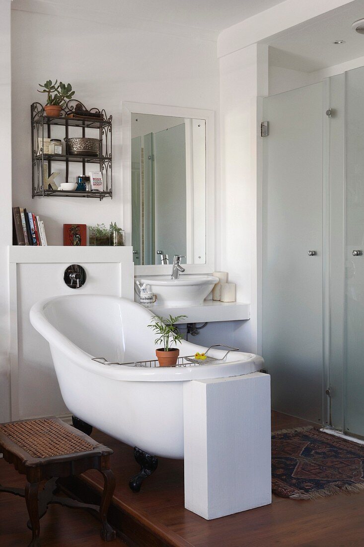 Free-standing vintage bathtub next to separate shower area with frosted glass doors in white bathroom