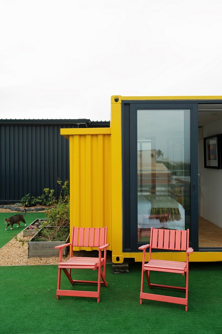 Garden chairs on artificial lawn in front of yellow shipping-container home