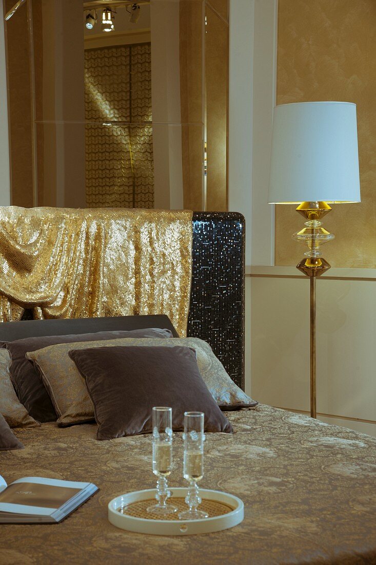 Elegantes Doppelbett mit übergehängtem, goldglitzerndem Stoff, daneben Stehlampe