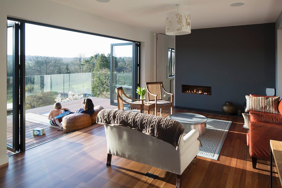 Elegant, traditional interior with leather sofa, antique chairs and dark grey wall; family sitting in warm spring sunshine on balcony with view of landscape