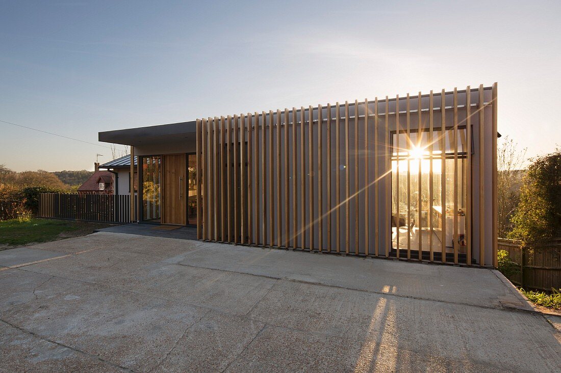 Sun setting behind modern, architect-designed house with wooden slatted structure on facade