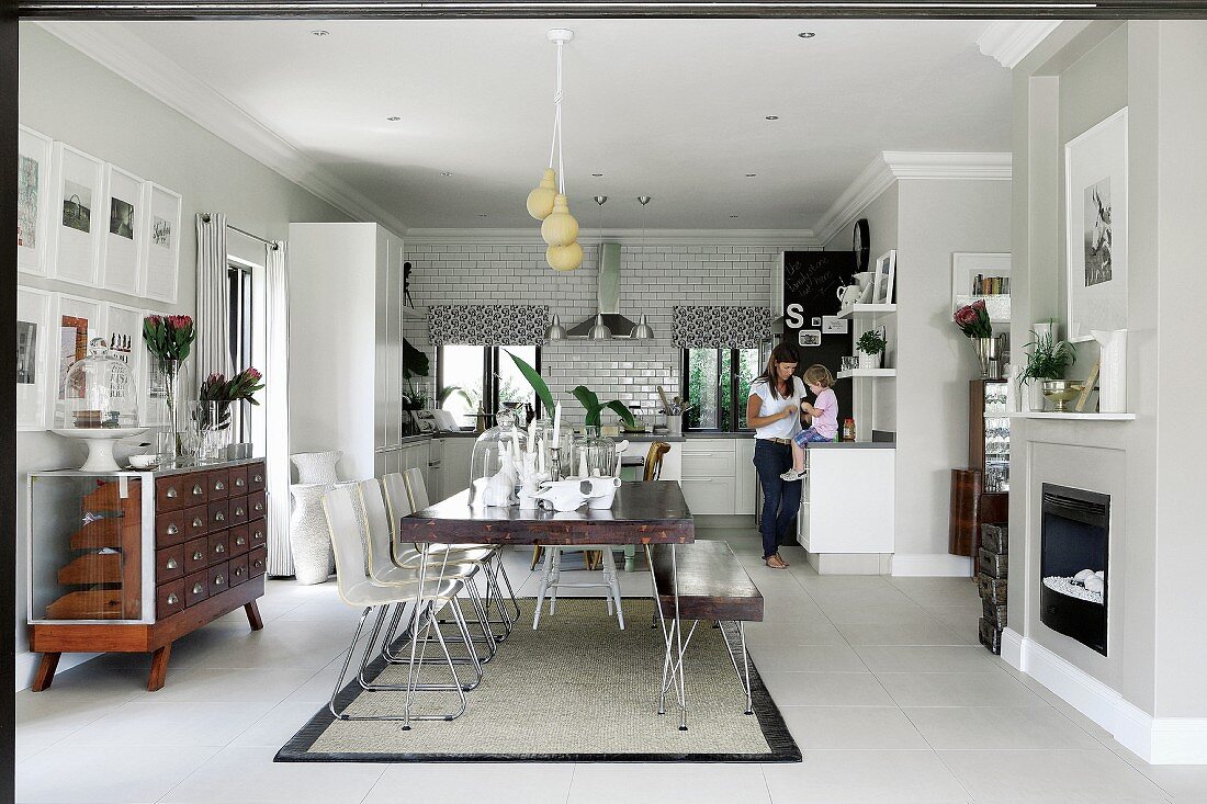Esstisch mit passender Bank und weissen Stühlen in offenem Wohnraum, im Hintergrund Familie in der Küche