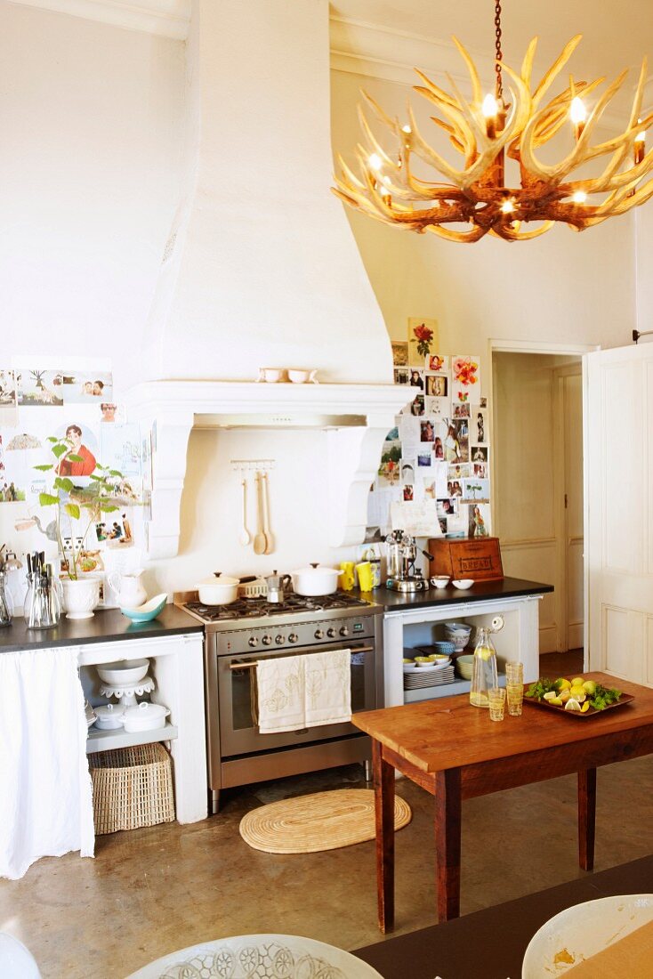 Holztisch vor Küchenzeile mit Gaskochherd unter gemauertem Dunstabzug in traditioneller Küche mit Geweihleuchter und Wanddekoration