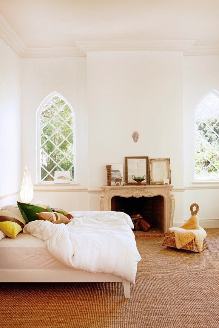 Doppelbett mit weisser Bettwäsche in traditionellem Schlafzimmer mit Sisal-Teppichboden, im Hintergrund Spitzbogenfenster mit Gitter