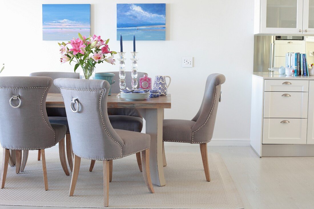 Elegant upholstered chairs, lilies and crockery on table in elegant dining area