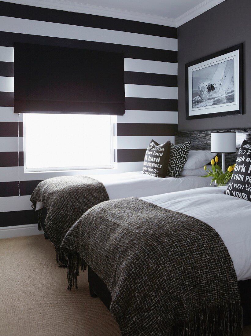 Twin beds, accent wall in wide black and white stripes and black fabric roller blind in small bedroom