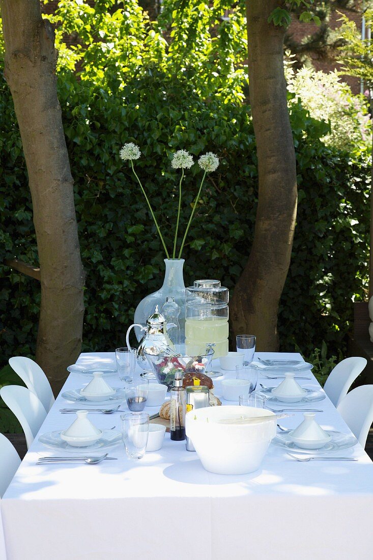 Gedeckter Tisch mit weisser Tischdecke, im Garten unter schattigen Bäumen