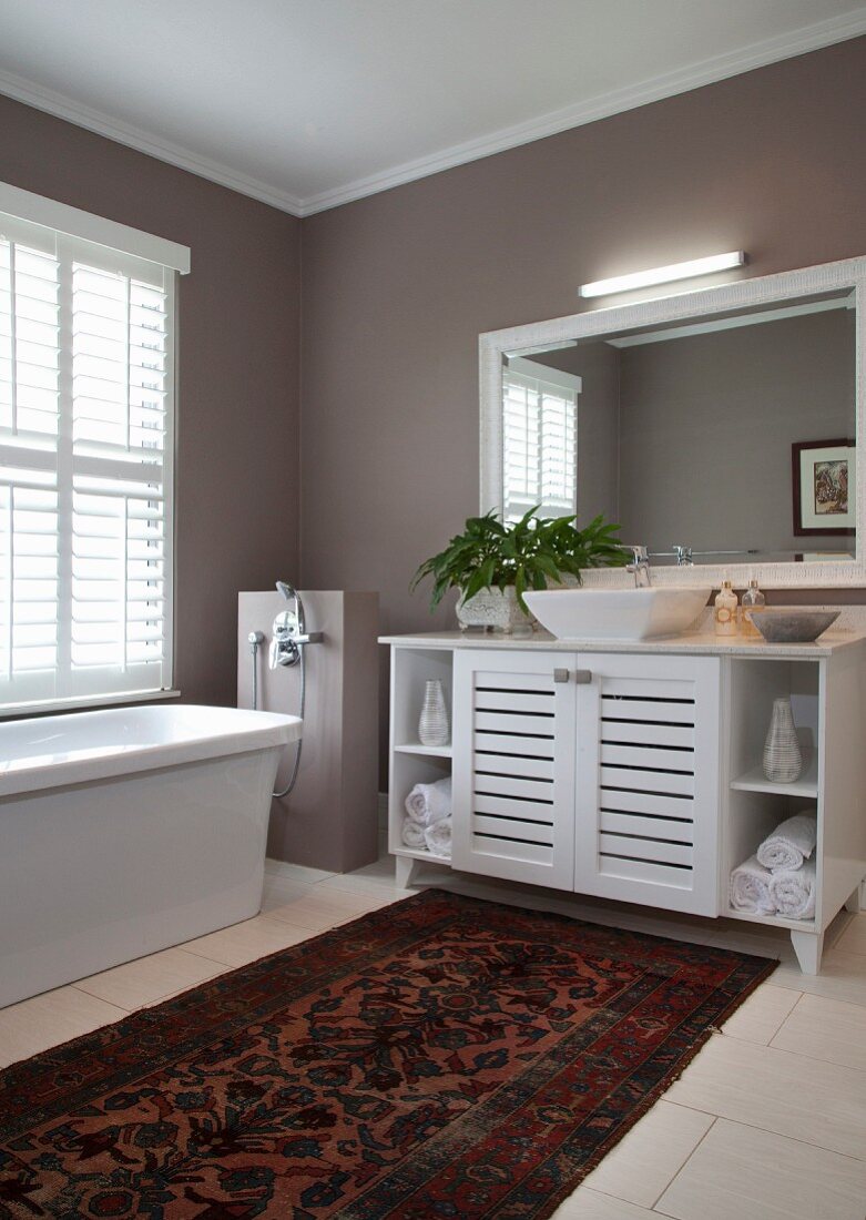 Elegant bathroom with taupe walls, rug, washstand and floor-mounted bathtub taps