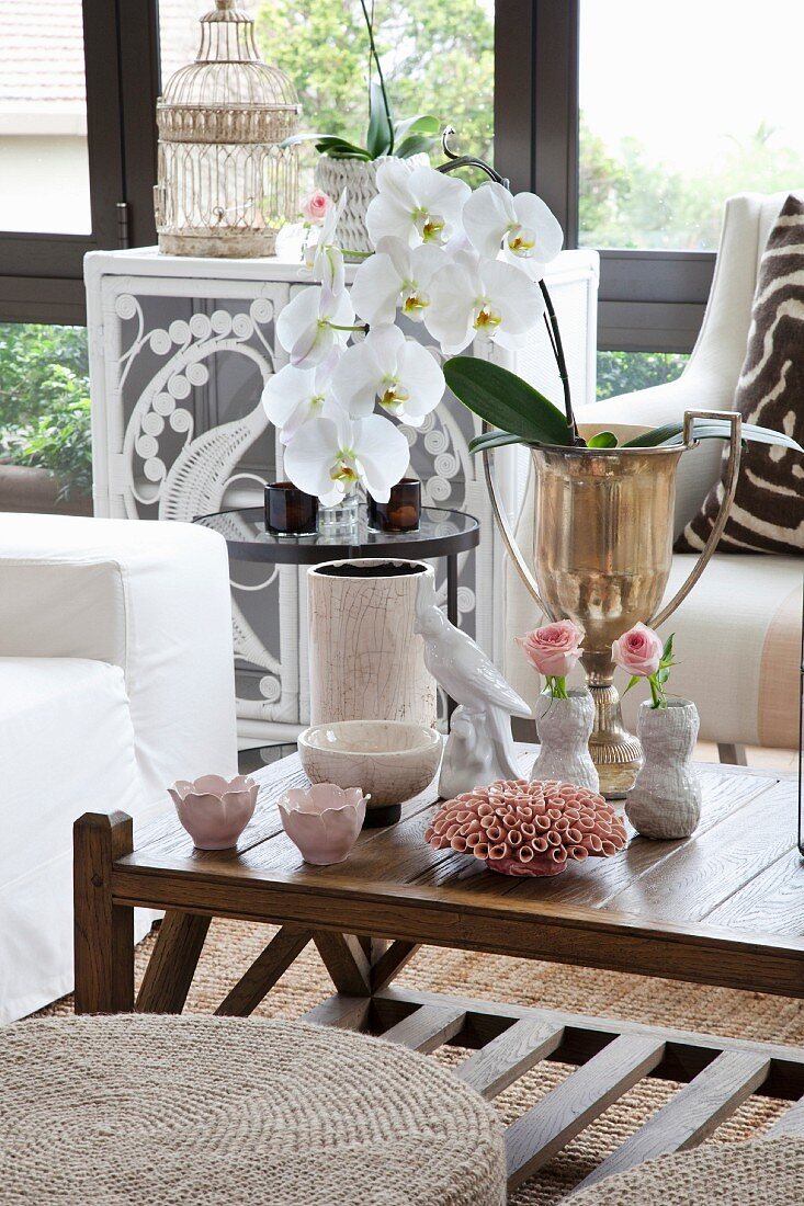 weiße Orchidee in vergoldeten Pokal und verschiedene Vasen auf Couchtisch