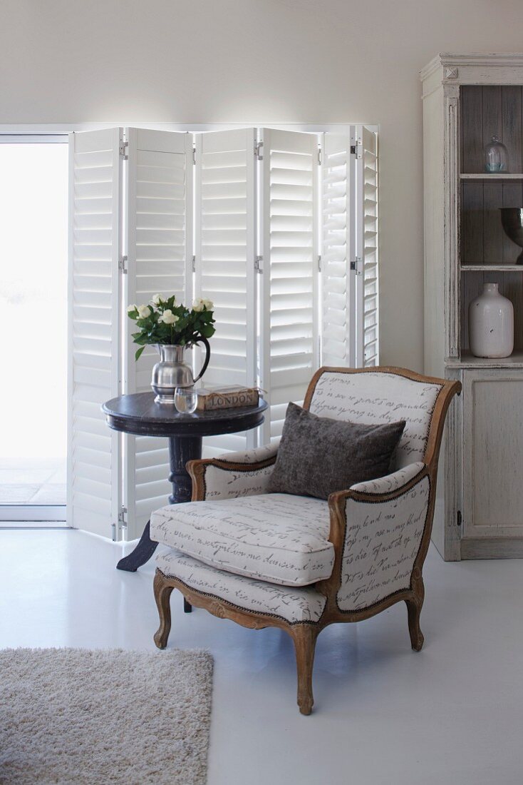 Antique armchair next to bistro table in front of white shutters on terrace doors