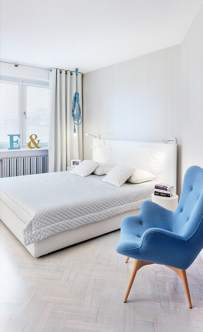 Blue retro armchair next to double bed with white headboard in modern bedroom