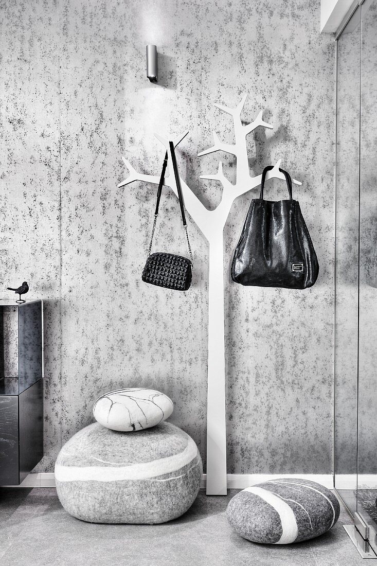 Floor cushions and bags hung on stylised tree as coat rack against wallpapered wall