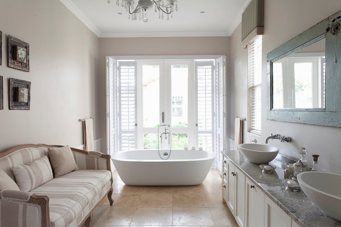 Comfortable sofa in spacious bathroom with free-standing bathtub in front of French windows in background