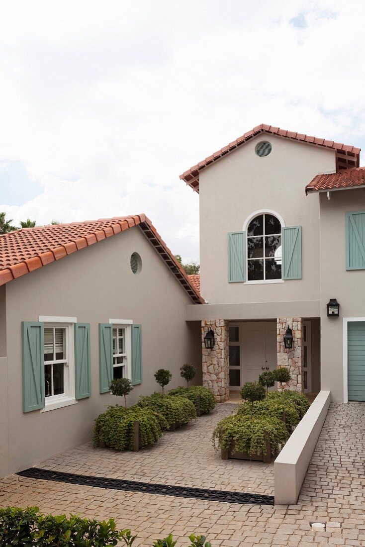 Wohnhaus mit sandfarbener Fassade und pastellgrünen Fensterläden, Pflanzkübel auf Pflasterboden vor Eingang