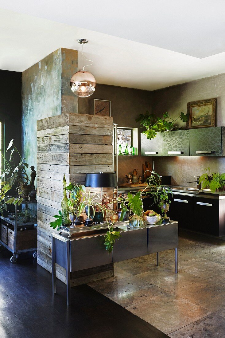 Various rustic and stainless steel materials in interior with open-plan kitchen and foliage plants