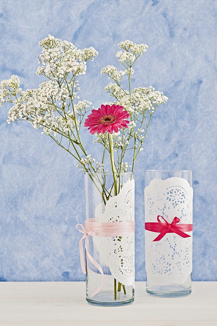 Doilies tied around simple, cylindrical vases with silk ribbons