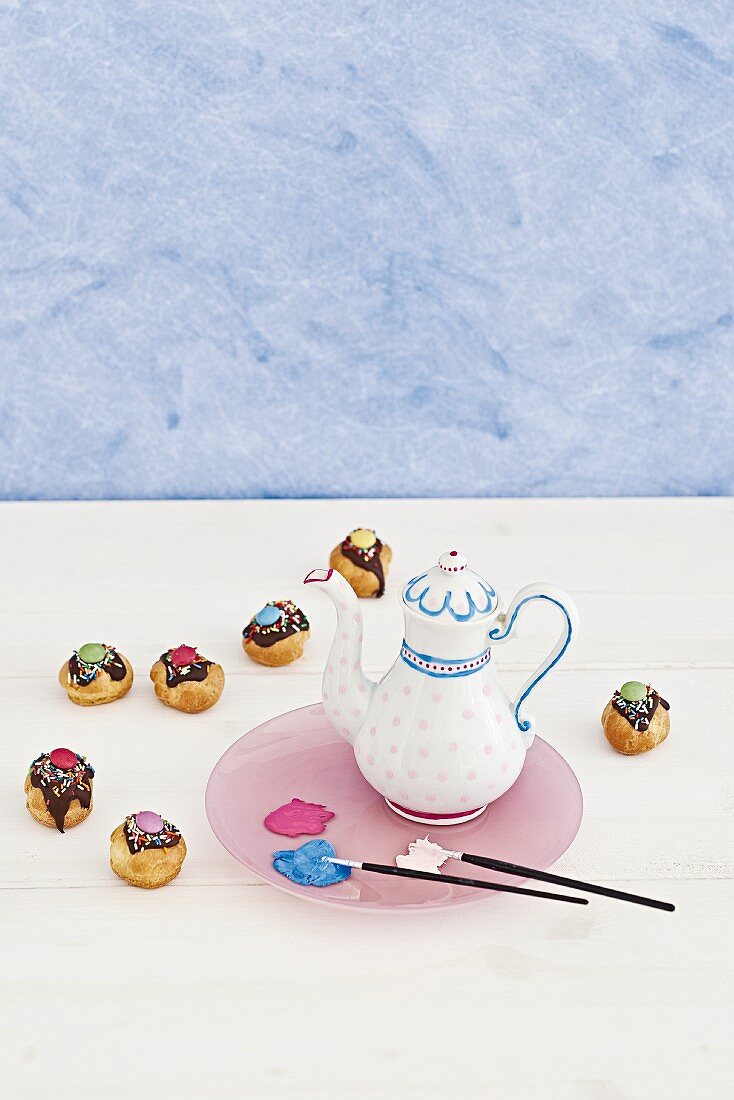 Pinsel und mit Porzellanfarben bemalte Kaffeekanne, bunt verzierte Cake Pops