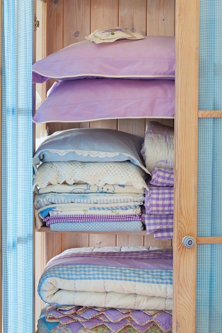 Heller Holzschrank mit gestapelter Bettwäsche und Kopfkissen in Pastelltönen