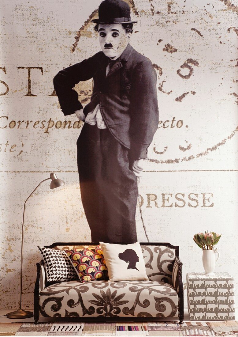 Tapete mit Charlie Chaplin Motiv, davor Sofa mit gemustertem Stoffbezug und Retro Stehleuchte