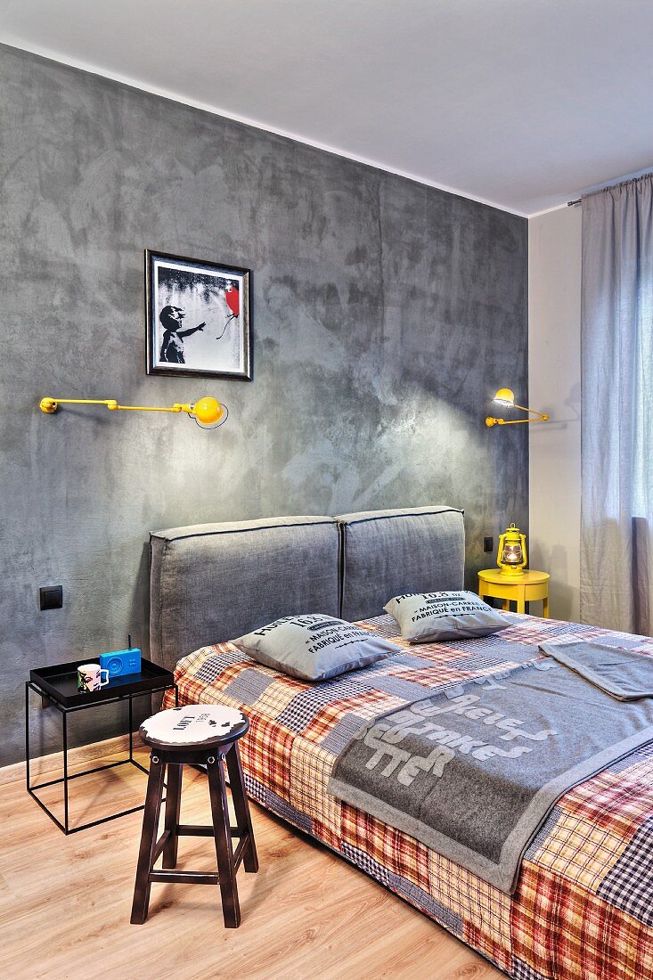 Concrete-grey bedroom with yellow accents and patchwork cover on double bed