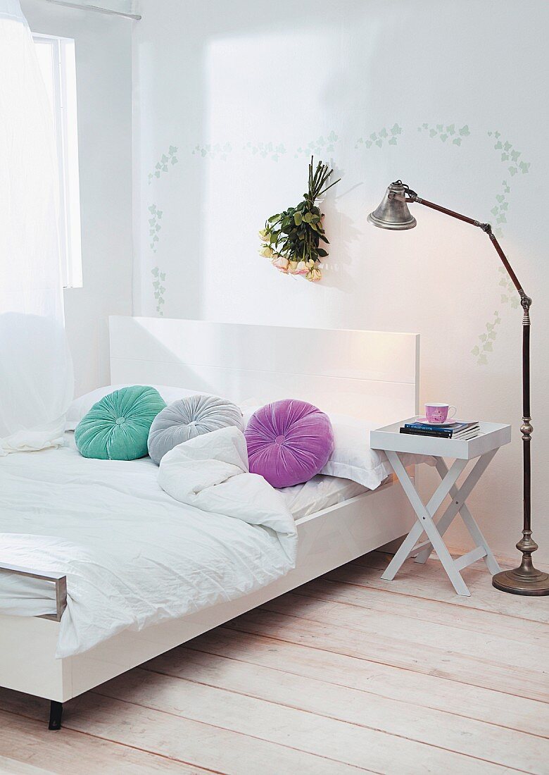 Modernes Doppelbett mit weißem Kopfteil und runde, farbige Kissen, seitlich klappbarer Beistelltisch neben Retro Stehleuchte