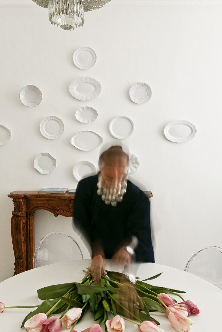 Verschwommene Frau legt Tulpen auf einen Tisch, vor einer Kaminkonsole und Wandtellern